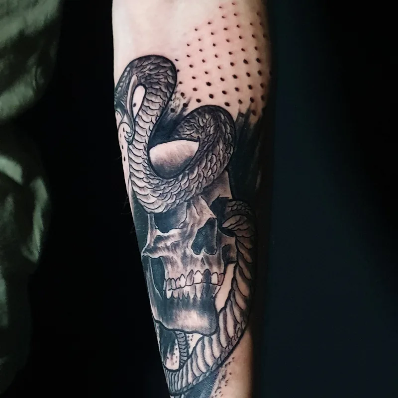 Serpent enroulé autour d'un crâne, en noir et gris avec des points, sur l'avant-bras, tatouage trash polka